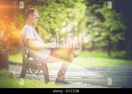 Outdoor Office Laptop Work. Men Working on His Laptop Computer in the Park During Sunny Summer Day. Outdoor Creativity Stock Photo
