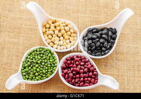 Multicolored beans in white ceramics spoon on sack background. Stock Photo