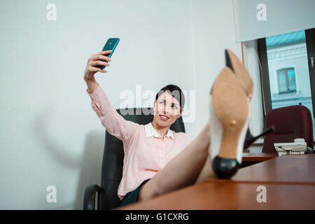Relaxed business woman sitting in a chair with legs over the table. Stock Photo