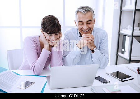 Office workers sitting at desk and surfing the web with a laptop, they are enjoying and watching funny videos online Stock Photo