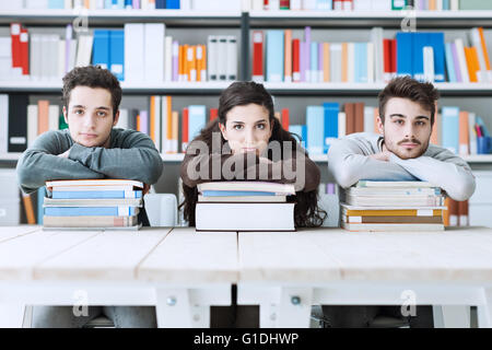 Young college students at the library studying together, they are leaning on a pile of books and looking at camera Stock Photo
