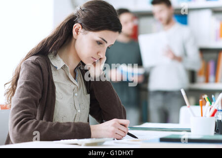 Young female student doing homework and studying at the library, students and bookshelves on background, education and learning Stock Photo