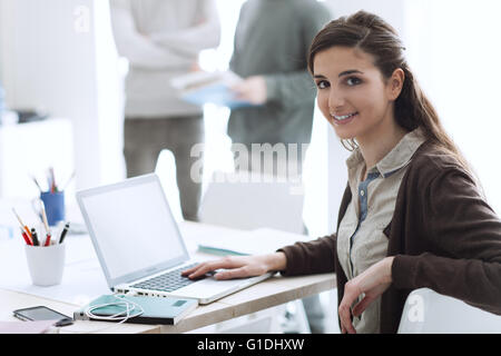 College students in the class, a girl is smiling at camera and using a laptop on foreground Stock Photo