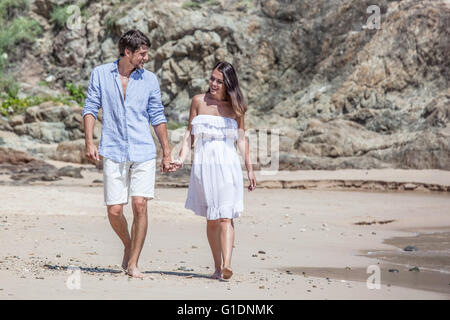 Young happy couple walking on beach smiling and holding hands Stock Photo