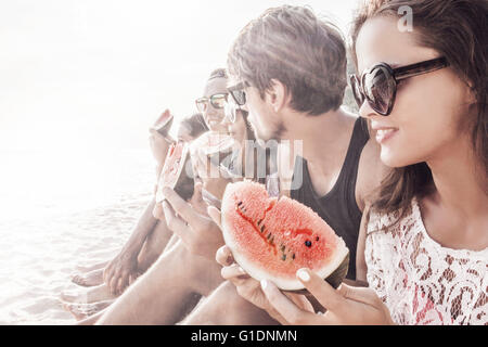 Group of young people sitting on beach and eating watermelon Stock Photo
