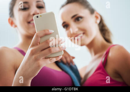Happy young girls at the gym using a fitness app on a smart phone, technology and training concept Stock Photo