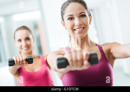 Teen sporty girls at gym exercising and weightlifting using dumbbells, body care and training concept