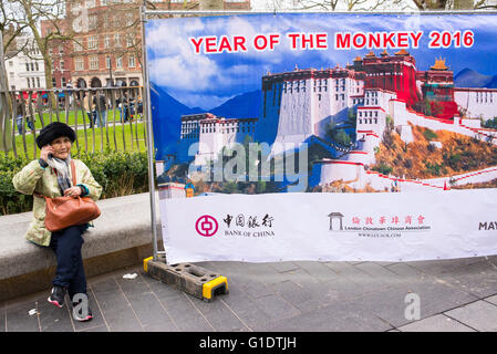 Big billboard celebrating Chinese New Year 2016, 'Year of the Monkey' with old Chinese woman on the phone sitting next to it. Stock Photo