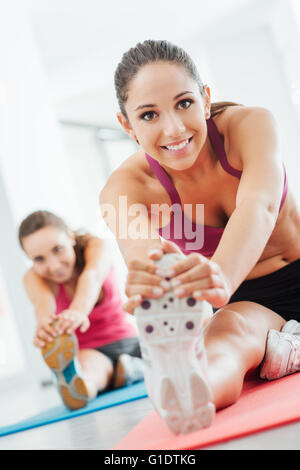 Smiling young women at the gym doing a stretching exercise for legs on a mat, fitness and health concept Stock Photo
