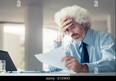 Confused shocked businessman receiving bad news, reading a letter and touching his forehead, failure and loss concept Stock Photo