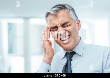 Suffering businessman having a terrible headache and touching his temples, stress and illness concept Stock Photo