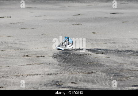 Shoe left on the beach between low and high tide marks, water ebbing and flowing left patterns on the sand due to this obstacle Stock Photo