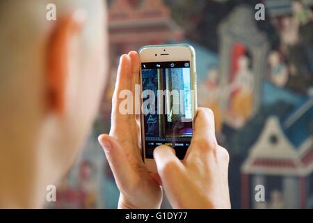 A woman photographs wall paintings at the chapel of the reclining Buddha, Wat Pho, Thailand Stock Photo