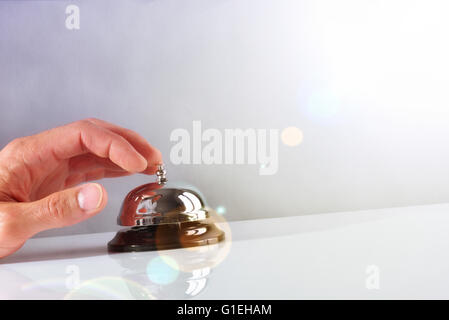 Hand of a Customer ringing the bell hotel service on a table white glass. Concept hotel, travel, room. Front view Stock Photo