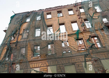 Old living house is under reconstruction, facade with empty windows is covered with green protection mesh Stock Photo