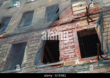 Old living house is under reconstruction, red brick wall covered with green protection mesh Stock Photo