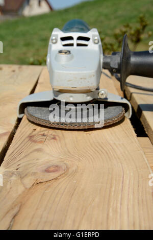 Angle grinder with abrasive disc on plank after work. Blurred background. Focus on wood. Shallow depth of field. Stock Photo