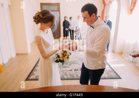 Smiling bridegroom putting the wedding ring on his wifes finger Stock Photo