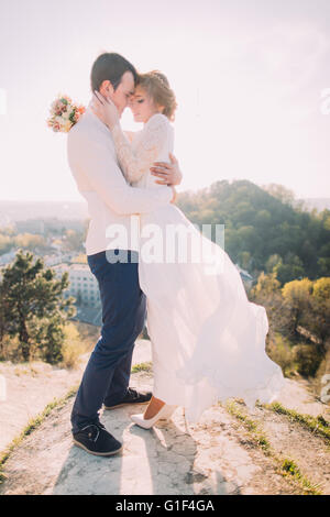 Attractive young loving couple of groom  and gentle bride wearing white dress fluttering in the wind standing on sunny outdoor background Stock Photo