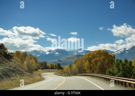 a winding mountain road goes between yellow aspen trees towards distant mountains Stock Photo