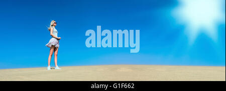 MODEL RELEASED. Young woman standing on sand against clear blue sky. Stock Photo