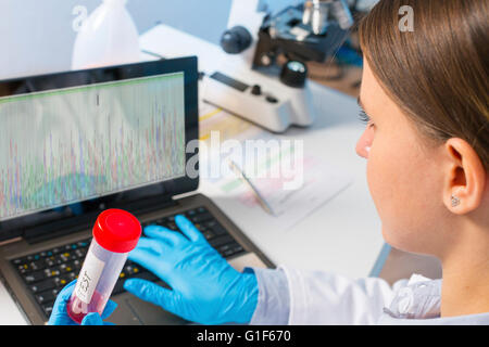 MODEL RELEASED. Female lab technician using laptop and holding test tube. Stock Photo
