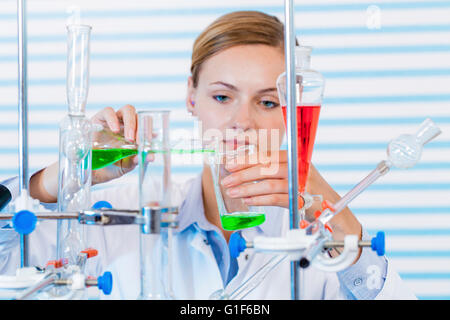 MODEL RELEASED. Female chemist pouring chemicals into glassware in laboratory. Stock Photo