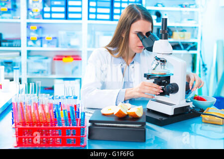 MODEL RELEASED. Female scientist studying food samples under a microscope. Stock Photo