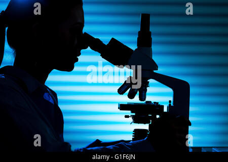 MODEL RELEASED. Silhouette of a female scientist using a microscope. Stock Photo