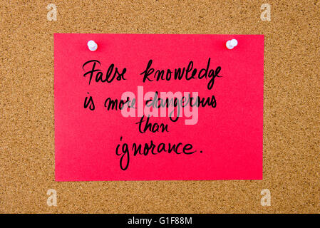 Red paper note with handwritten text False Knowledge Is More Dangerous Than Ignorance pinned on cork board with white thumbtacks Stock Photo