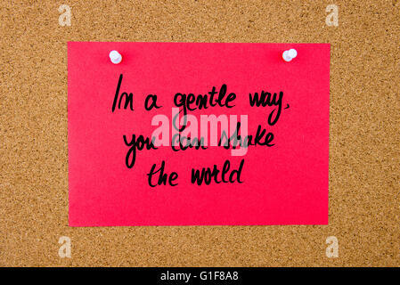 Red paper note with handwritten text In A Gentle Way You Can Shake The World pinned on cork board with white thumbtacks Stock Photo