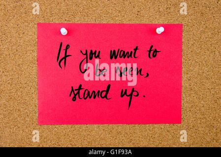 Red paper note with handwritten text If You Want To Be Seen, Stand Up pinned on cork board with white thumbtacks Stock Photo