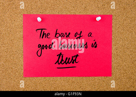 Red paper note with handwritten text The Base Of A Good Business Is Trust pinned on cork board with white thumbtacks Stock Photo