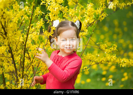 Child playing hide and seek. Beautiful little girl hiding behind tree in spring blossoms. Small kid looking at camera Stock Photo