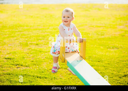 Little girl enjoying riding swing with mum at beautiful nature background. Baby happily playing with parents outside Stock Photo