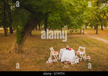 Beautiful photobooth in autumn city park. Festively decorated white wooden chairs and table in scenic place. Image toned and sty Stock Photo