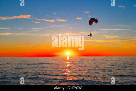 Silhouette of paraglider flying over sea at sunset Stock Photo