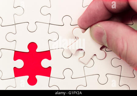 still life with a white jigsaw/puzzle incomplete over a red background, symbol of problem solving Stock Photo
