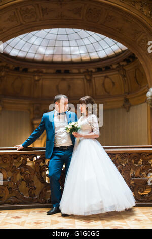 Happy groom and bride embracing in the front of old stained-glass ceiling at rich wooden interior Stock Photo