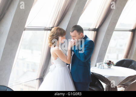 Groom gently kissing hand of his lovely bride in modern interior Stock Photo