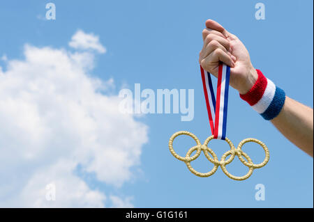 RIO DE JANEIRO - FEBRUARY 4, 2016: Hand with red white and blue wristband holding gold Olympic rings medal hanging from ribbon. Stock Photo