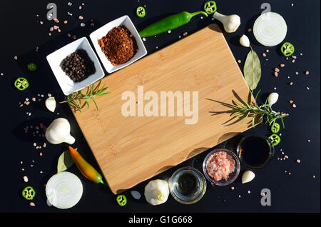 Food background. Empty cutting board and pepper, bay leaf, rosemary, onions, Himalayan salt, olive oil, soy sauce on a black Stock Photo