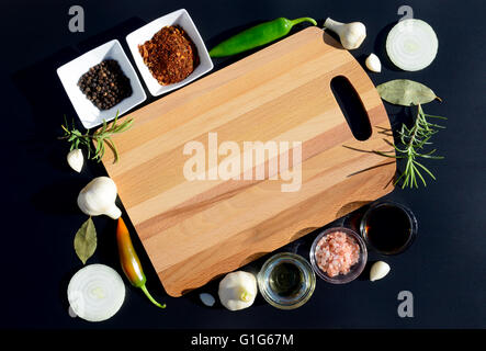 Food background. Empty cutting board and pepper, bay leaf, rosemary, onions, Himalayan salt, olive oil, soy sauce on a black Stock Photo