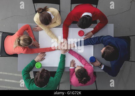 Group of people joining hands in stack sitting around the table Stock Photo