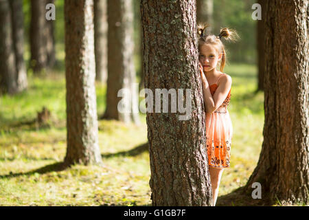 Ten-year-old girl looks out from behind a tree. Stock Photo