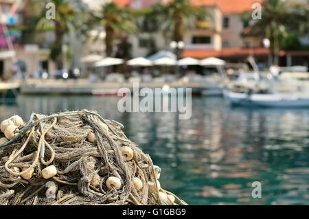 Pile of fishing nets with floats on a quay with blurred boats on background. Podgora, Croatia Stock Photo