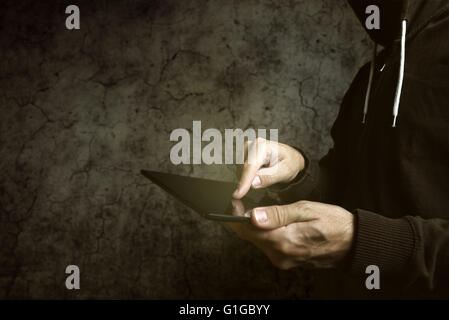 Faceless hooded unidentifiable male person using tablet computer, internet hacker and online security concept. Stock Photo