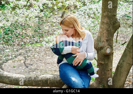 mother with her baby son sitting on tree branch in spring garden Stock Photo