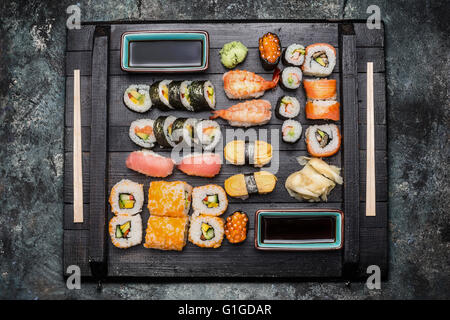 Sushi Set: maki, nigiri , ouside rolls  served with  soy sauce , pickled ginger and wasabi on dark wooden plate , top view Stock Photo