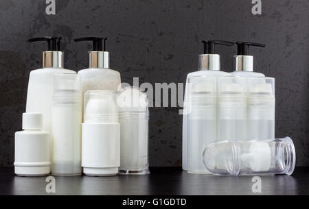 Six full and six empty beauty product plastic bottles on a dark wooden table with a gray textured background. Stock Photo